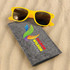 A pair of yellow sunglasses resting on a gray case, with a colorful logo on the case.