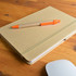 A beige notebook with an elastic band and an orange pen placed on a wooden surface.