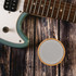 A round white Bluetooth speaker with a wooden base, placed beside a teal electric guitar on a rustic wooden surface.