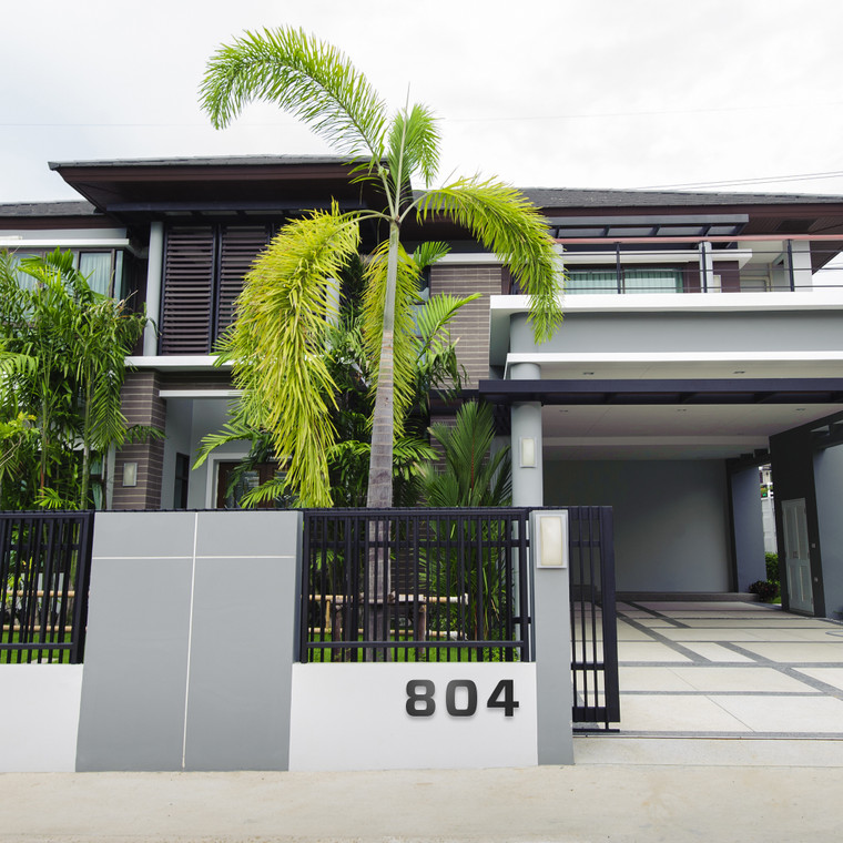 Modern house in grey and white stucco with horizontal wood siding. A large palm tree and modern front gate with bold modern house numbers on pony wall.