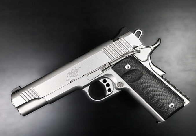 Stainless steel 1911-style semi-automatic handgun with black grips resting on a tree stump alongside a chain and spent shell casings.