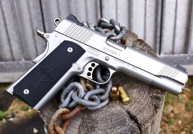 Stainless steel 1911-style semi-automatic handgun with black grips resting on a tree stump alongside a chain and spent shell casings.