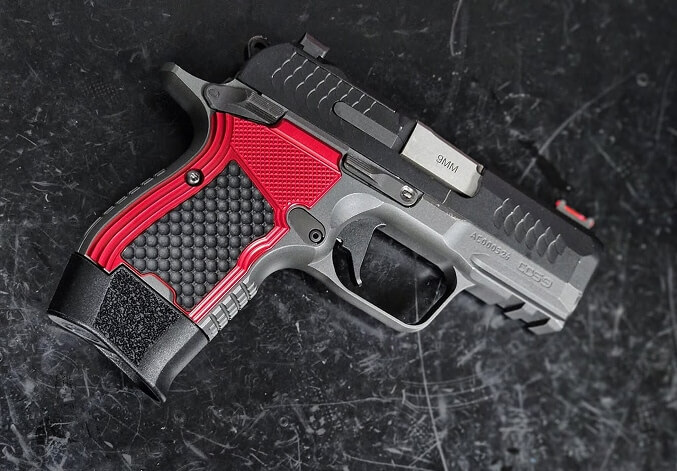 Stainless steel 1911-style semi-automatic handgun with black grips resting on a tree stump alongside a chain and spent shell casings.