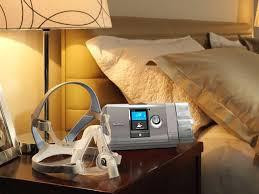Resmed AirCurve 10 CS PaceWave, medical device used for sleep apnea therapy placed on bedside table in a bedroom setting.