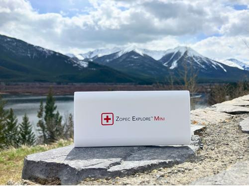 Zopec Explore Mini, portable power bank with logo, placed outdoors on a rock with scenic mountain and lake background.