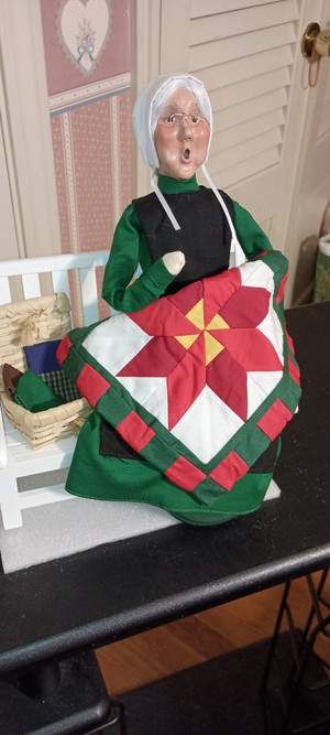 BYERS CHOICE CAROLER-2025- AMISH GRANDMOTHER ON BENCH-NEW