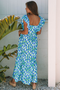 A stylish woman wearing a blue floral maxi dress featuring a square neckline and ruffle straps. The dress has a flowy, lightweight design with a flattering fit, perfect for summer, vacations, beach outings, or casual chic everyday wear. Available at LuxeUp.