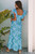 A stylish woman wearing a blue floral maxi dress featuring a square neckline and ruffle straps. The dress has a flowy, lightweight design with a flattering fit, perfect for summer, vacations, beach outings, or casual chic everyday wear. Available at LuxeUp.