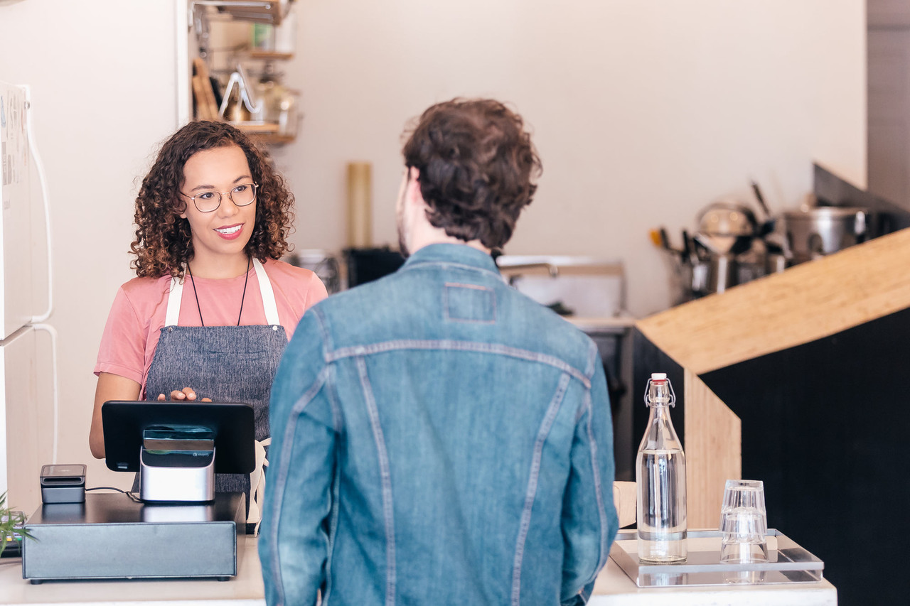 A shop colleague handing an order across the counter to a customer