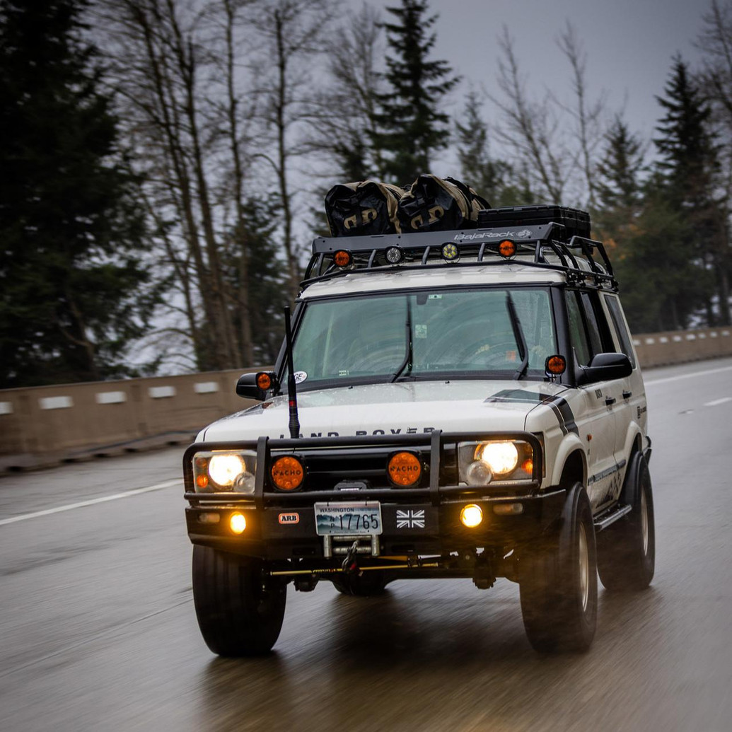 ARB Deluxe Winch Bumper 3432060B, vehicle front view with off-road equipment and accessories during drive on wet road.