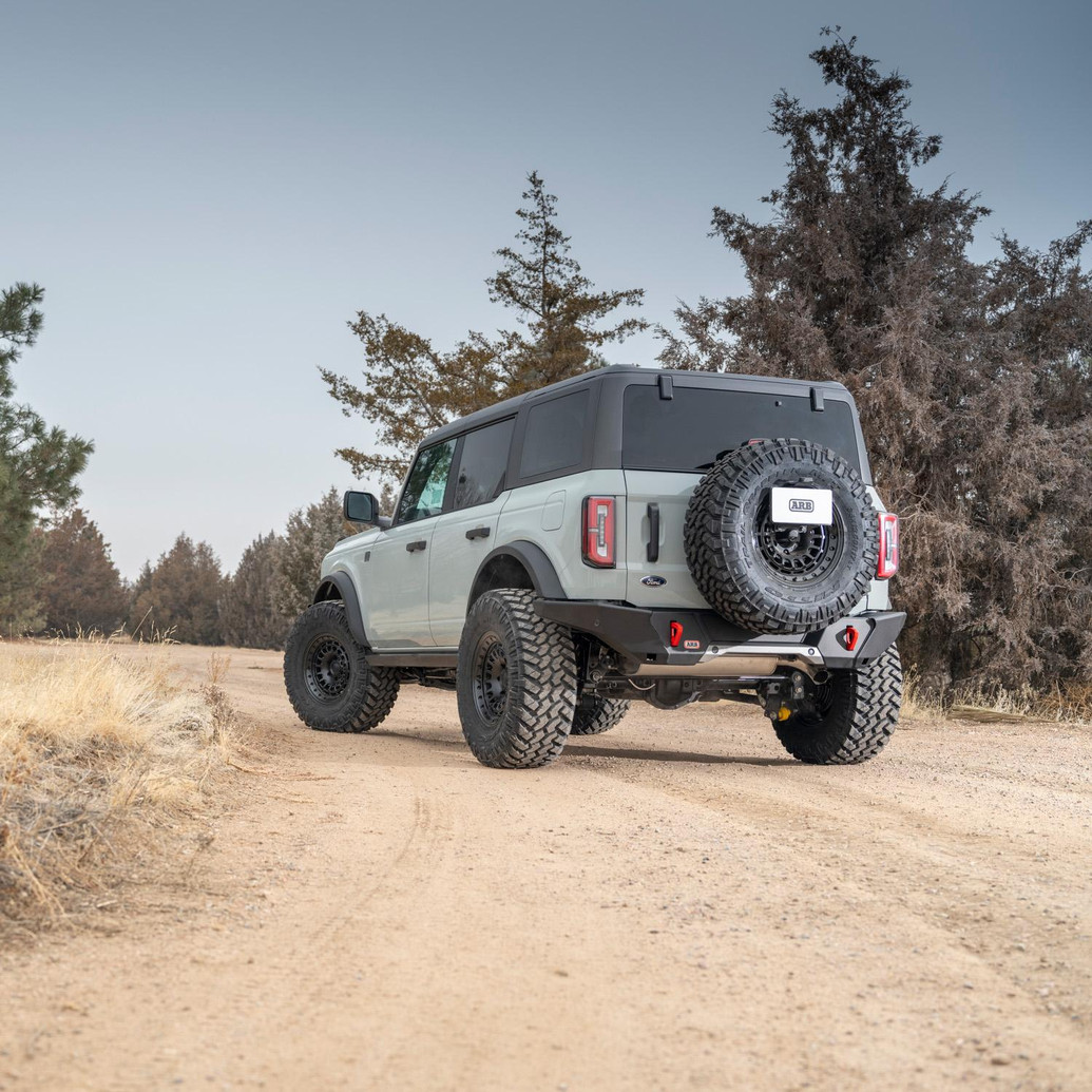 ARB Rear Zenith Bumper 5680020B, heavy-duty off-road rear bumper installed on a Ford Bronco, shown from the rear three-quarter view on a dirt trail.