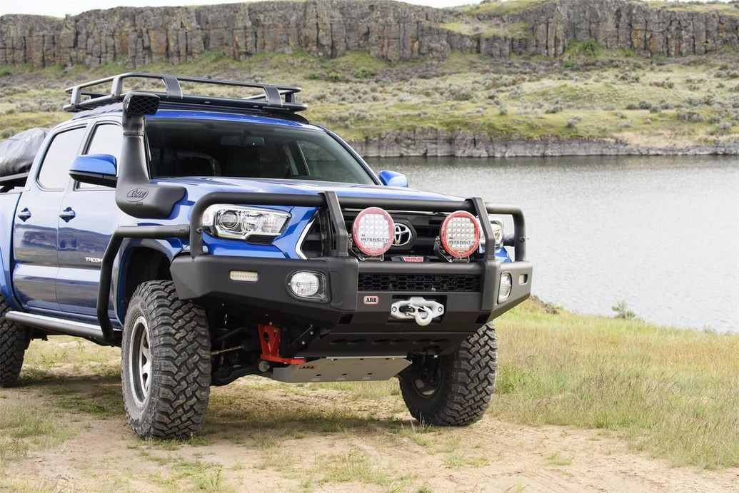 ARB Summit Bumper Kit 3423160KB, black off-road bumper with integrated winch mount, large fog lights, and mounting points for additional accessories on a blue Toyota Tacoma pickup truck.