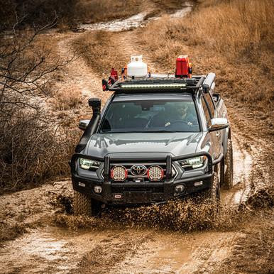 ARB Summit Bumper Kit 3423160K2B, rugged off-road vehicle driving through muddy terrain with front bumper and mounted accessories.