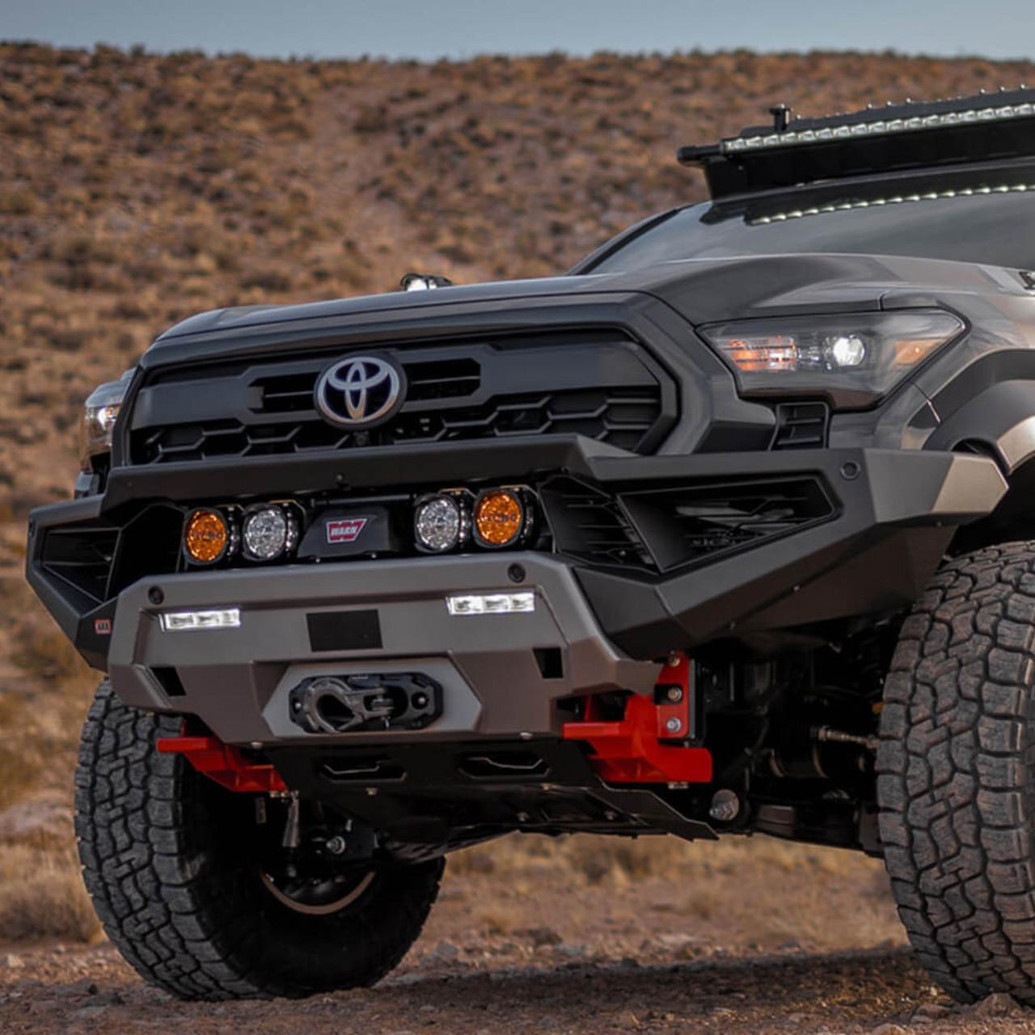 ARB Zenith Winch Bumper for Toyota Tacoma 2024+, front view of a rugged off-road vehicle with a black and gray bumper, integrated winch, and off-road lights in a desert landscape.