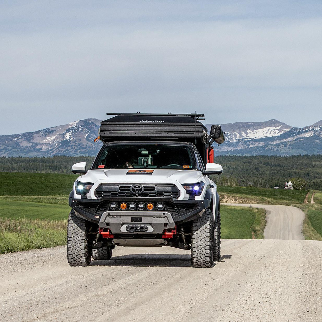 ARB Zenith Winch Bumper for Toyota Tacoma 2024+, front view of a rugged off-road pickup truck with the bumper equipped with a winch on a dirt road.