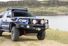 ARB Summit Bumper Kit 3423160KB, off-road vehicle bumper with a rugged black design, integrated winch, and auxiliary lights on a blue Toyota truck.