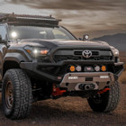 ARB Zenith Winch Bumper for Toyota Tacoma (2024+), black off-road style front bumper with integrated winch mount, four round auxiliary lights, and rugged design on a Toyota Tacoma vehicle in a desert setting.