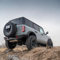 ARB Rear Zenith Bumper 5680020B, black off-road rear bumper installed on a gray Ford Bronco with a rear-mounted spare tire on rocky terrain.