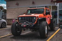 Poison Spyder Front JL/JT BRUISER Bumper in black on an orange Jeep Wrangler in a parking lot.