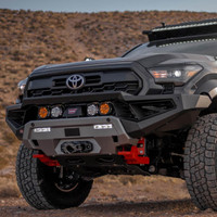 ARB Zenith Winch Bumper for Toyota Tacoma 2024+, front view of a rugged off-road vehicle with a black and gray bumper, integrated winch, and off-road lights in a desert landscape.