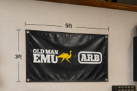Old Man Emu Shop Vinyl Banner 5'x3' 570195US, black banner with Old Man Emu and ARB logos, measuring 5 feet in width and 3 feet in height, hanging on a wall.