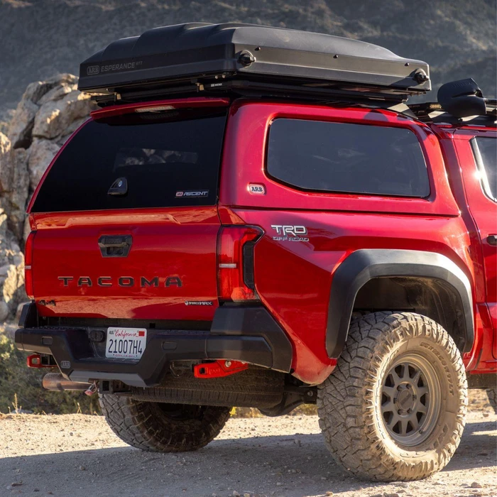 ARB Ascent Truck Cap for Tacoma 2024+, black truck bed cover on a red Toyota Tacoma pickup truck parked outdoors.