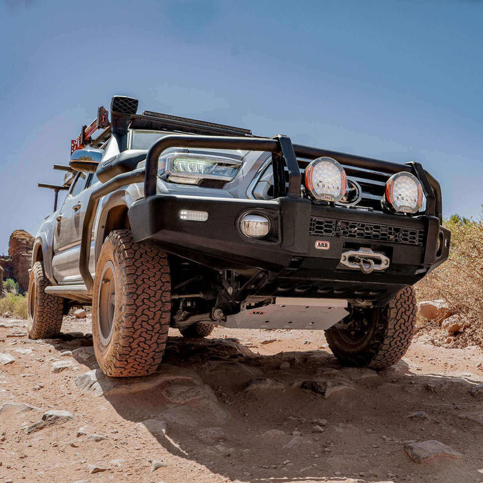 ARB Summit Bumper Kit 3423160K2B, rugged off-road vehicle bumper with integrated lights and winch mount on a 4x4 SUV in desert terrain.