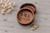 personalized round walnut wedding ring dish featuring custom engraved initials, a delicate floral design, couples' names, and wedding date. The natural walnut wood grain and engraved details are displayed alongside gold wedding rings. A beautiful wooden ring holder for wedding ceremonies, anniversaries, and personalized keepsake gifts.