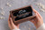 Personalized walnut wedding ring box with clear glass lid, shown held in hands to highlight its compact size and elegant craftsmanship. Features a custom UV-printed mountain design, personalized names and wedding date, and black velvet interior that holds 2–4 rings. Perfect for wedding ceremonies, ring bearers, anniversary gifts, Christmas gifts for your wife, Valentine's Day gifts for her, and personalized wedding keepsakes.