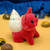 A red bear figurine with a white and blue speckled sea shell on it's back on a yellow and blue backdrop