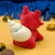 A red bear figurine with a white and blue speckled sea shell on it's back on a yellow and blue backdrop