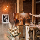Wedding photo canvas print displayed on a gold easel at a reception venue with floral arrangements and table settings