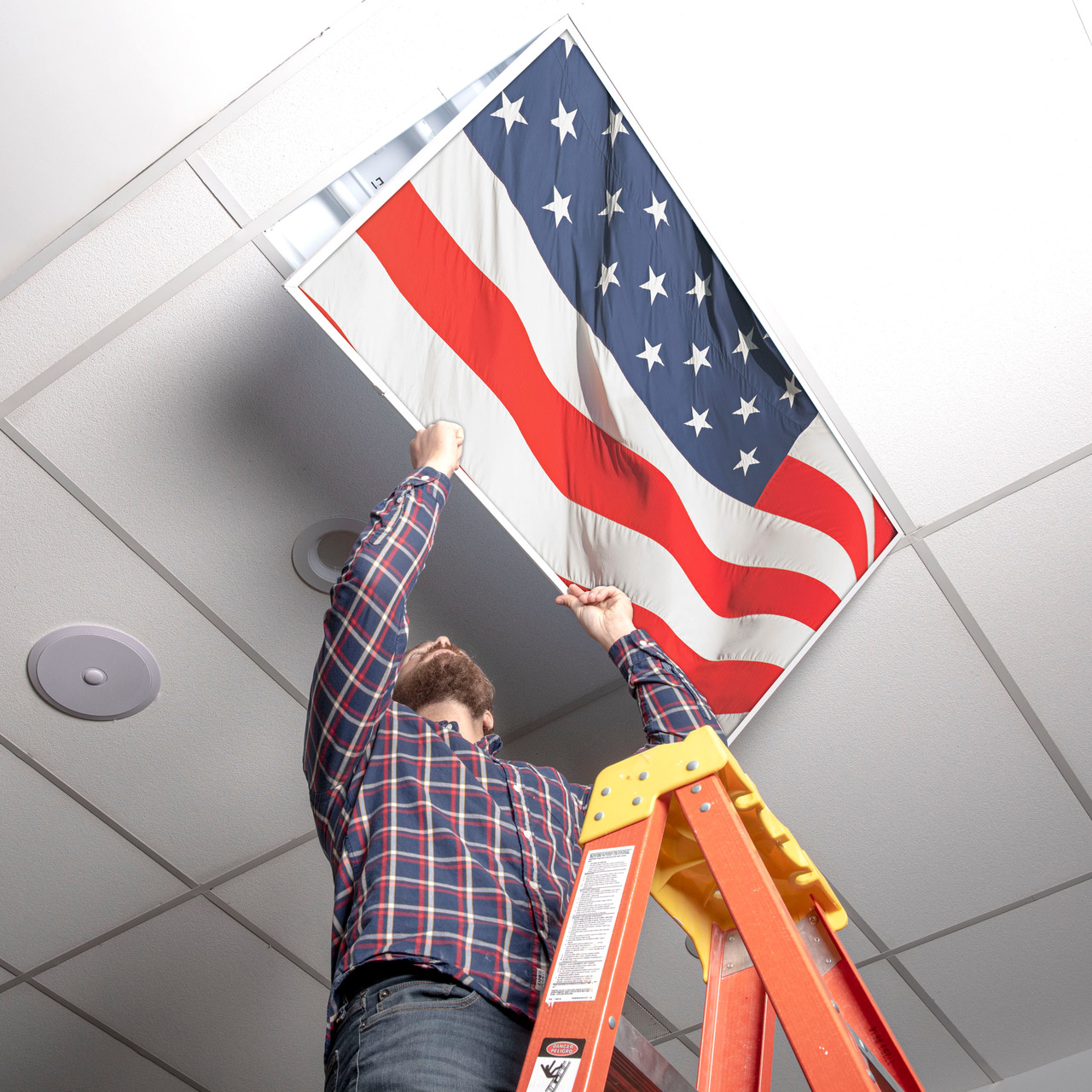 Installer placing an American flag light cover into a 2x4 ceiling fixture