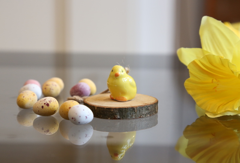 A table of mini chocolate eggs and a daffodil and a ceramic chick
