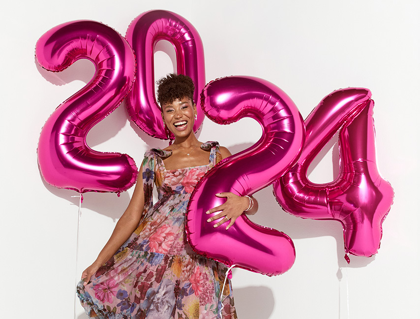 Girl standing in a dress holding balloons that show 2024.