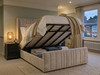 Front-opening beige velvet Carla Ottoman bed frame raised by a gas-lift mechanism to reveal a spacious under-bed storage area with solid base boards.