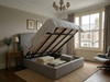 Melina Ottoman Storage Bed Frame upholstered in grey linen fabric, with the mattress base lifted open to reveal the internal under-bed storage area, featuring a curved wingback headboard.