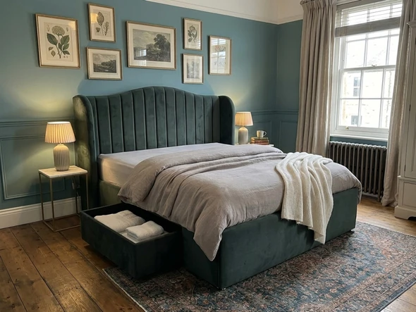 A Vendela fabric bed frame upholstered in green velvet, featuring a tall, winged headboard with deep fluted lines and a pull-out jumbo storage drawer at the base
