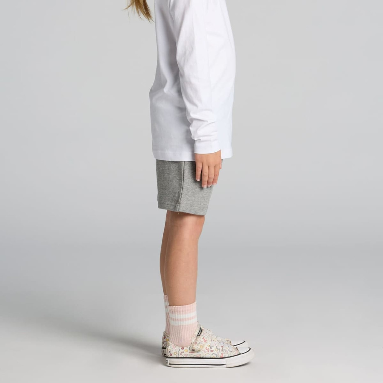 Kids stadium shorts in light grey, paired with a long-sleeve white top and patterned sneakers.