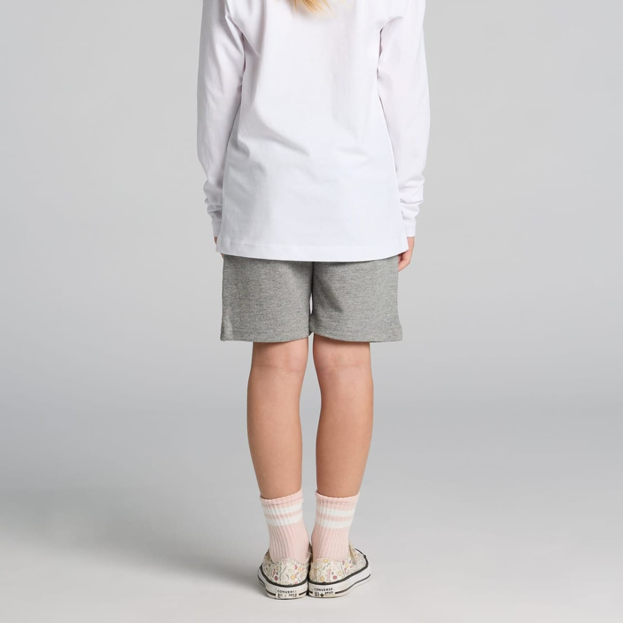 Kids stadium shorts in grey, featuring a simple design. Worn with a long-sleeve white top and patterned socks.