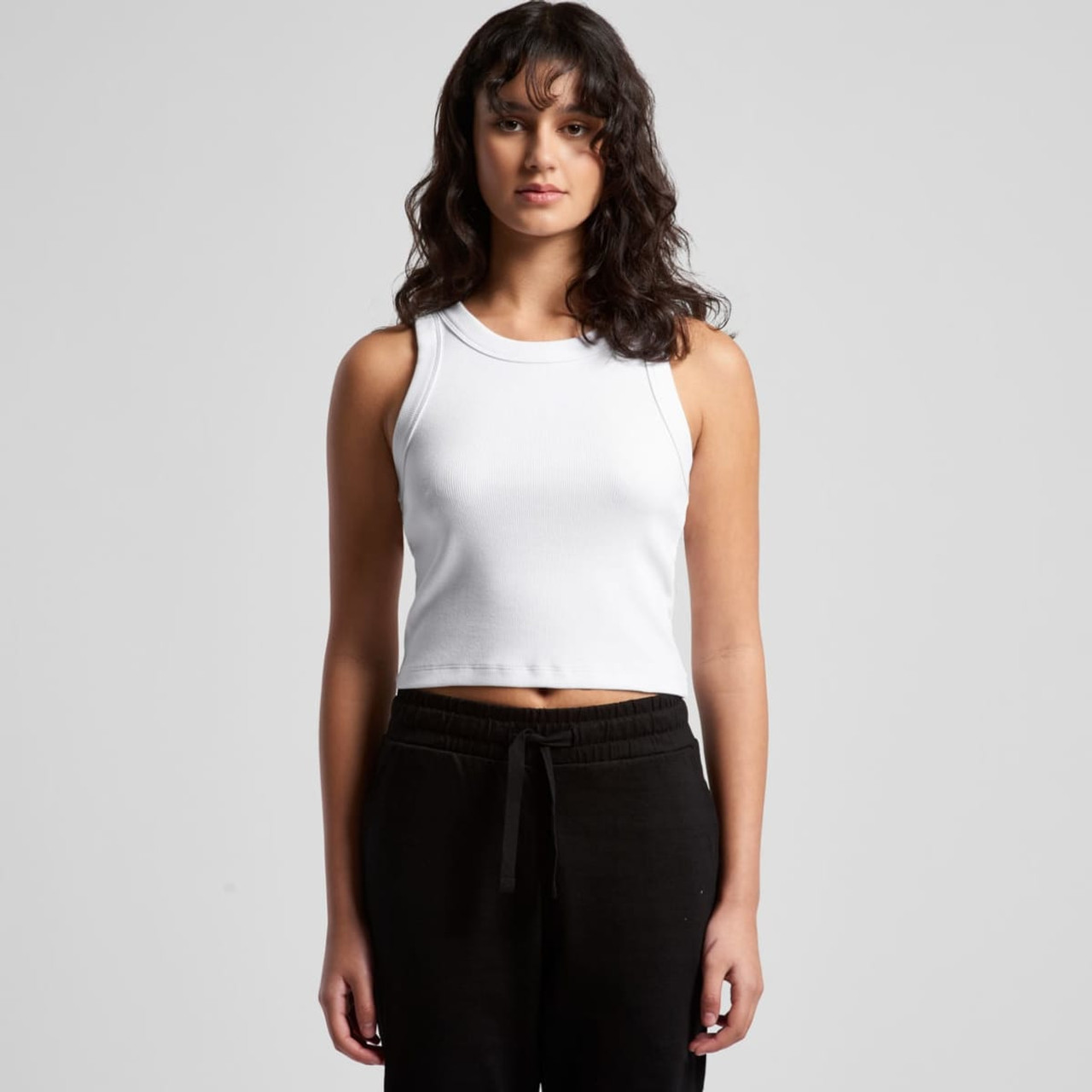 A white ribbed crop tank top worn by a model, paired with black pants. The top features a logo.