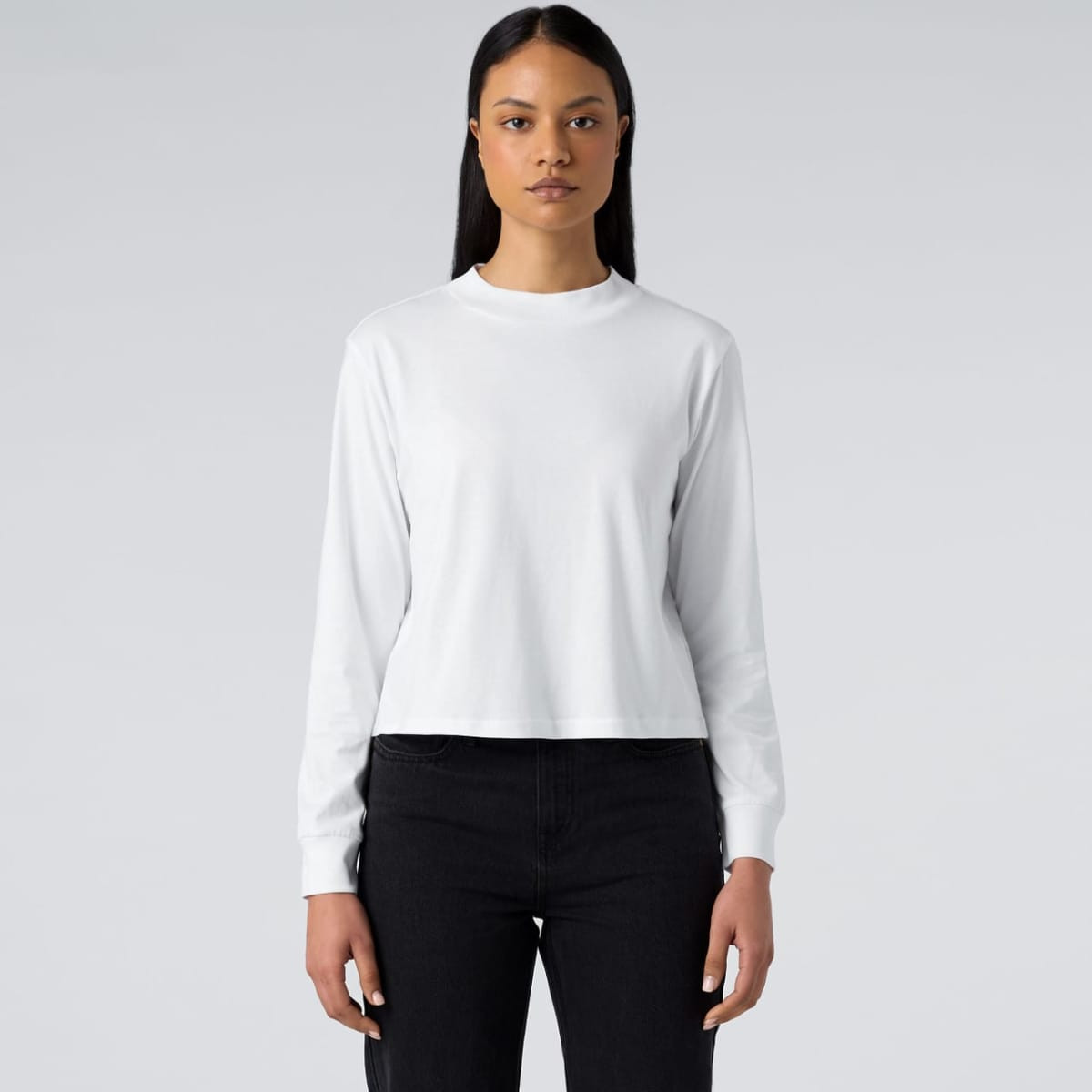 A white long sleeve tee, featuring a round neckline and a fitted design, worn with dark jeans.