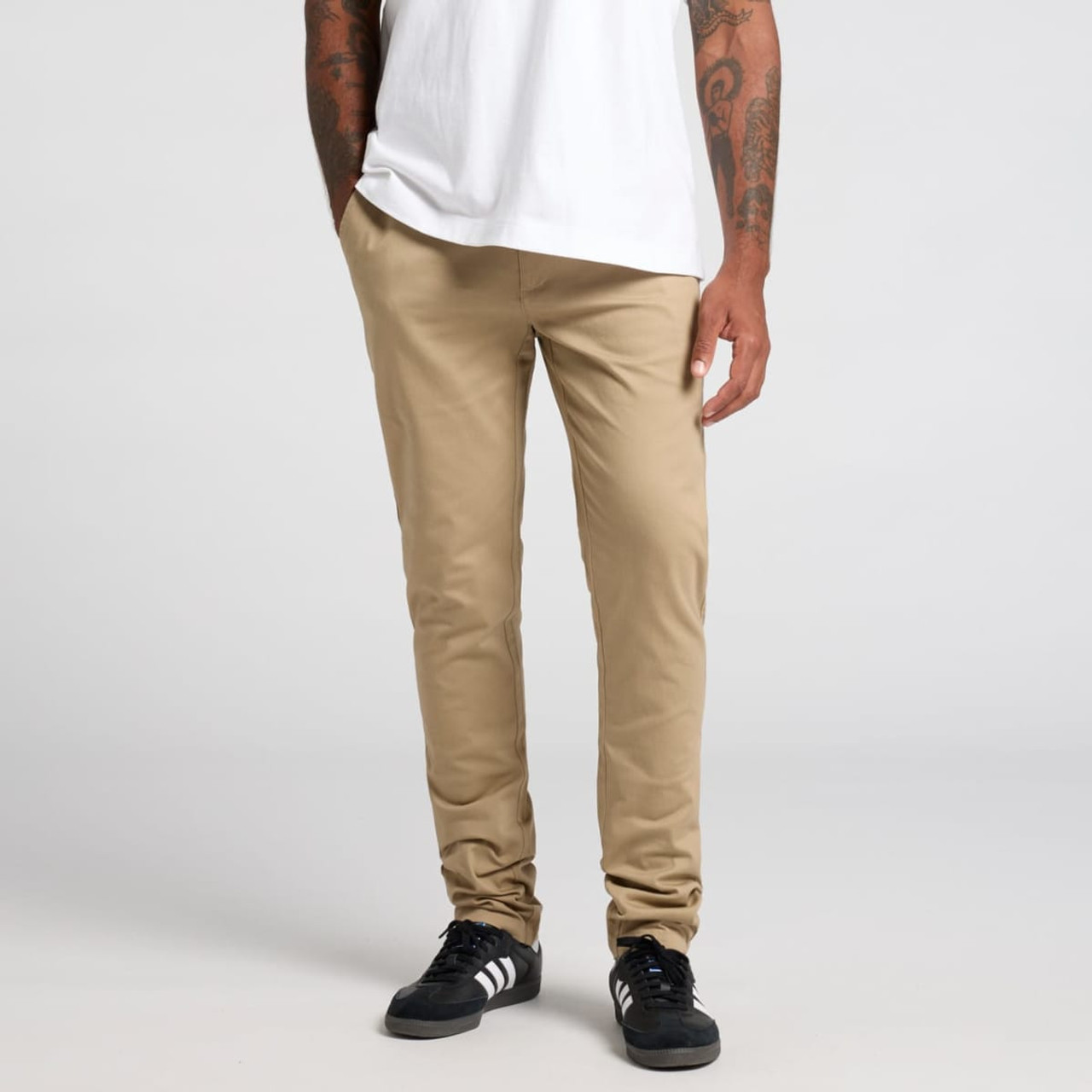 Beige pants are displayed on a model standing with hands in pockets, wearing a white t-shirt and black shoes.