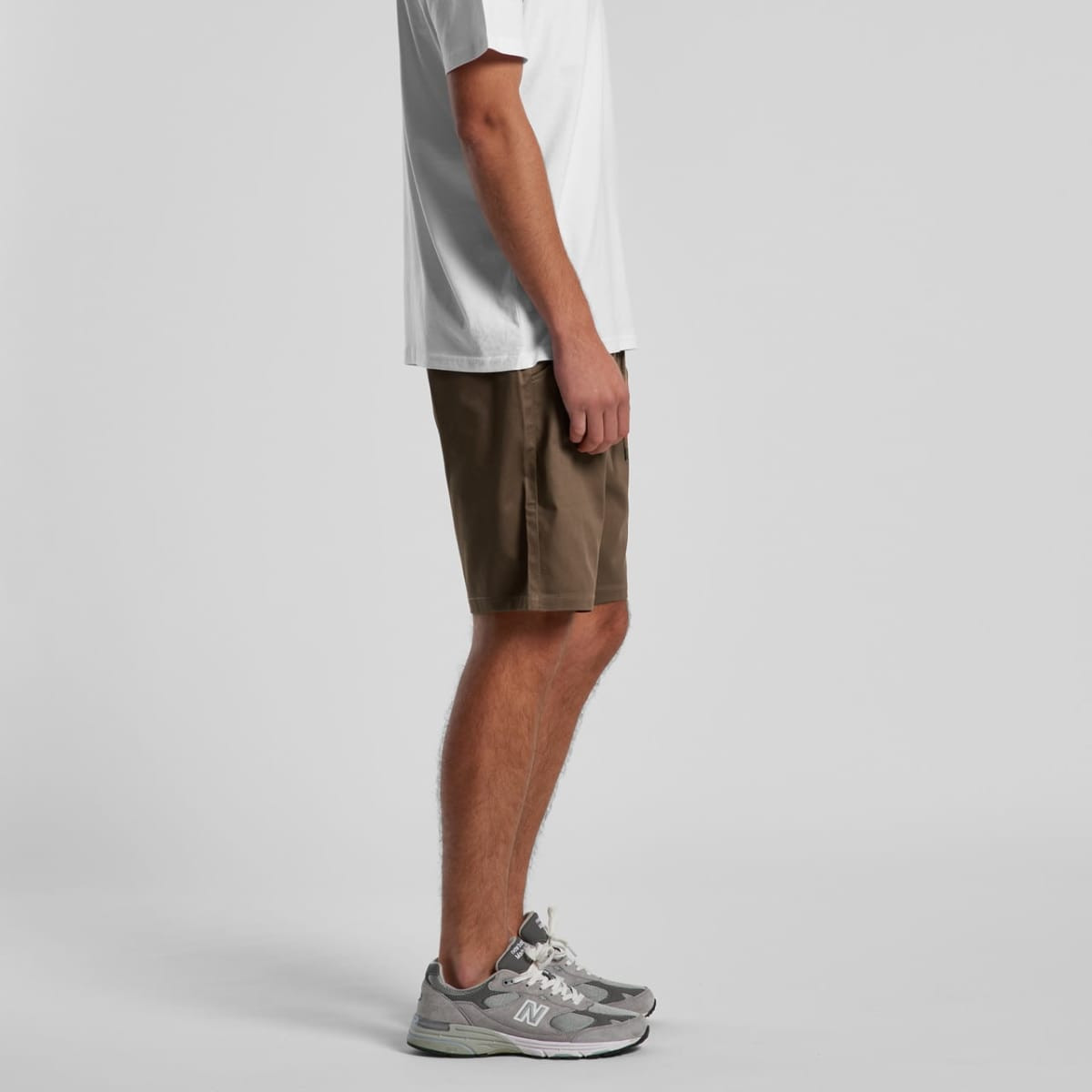 A pair of brown walk shorts with side pockets, displayed on a mannequin wearing a white T-shirt and grey sneakers.
