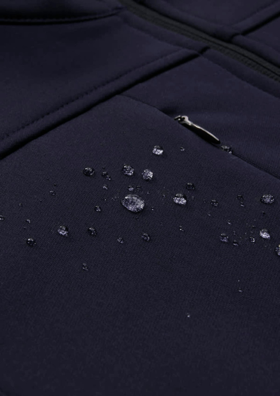 A dark navy softshell jacket with water droplets beading on the fabric, featuring a zippered pocket.