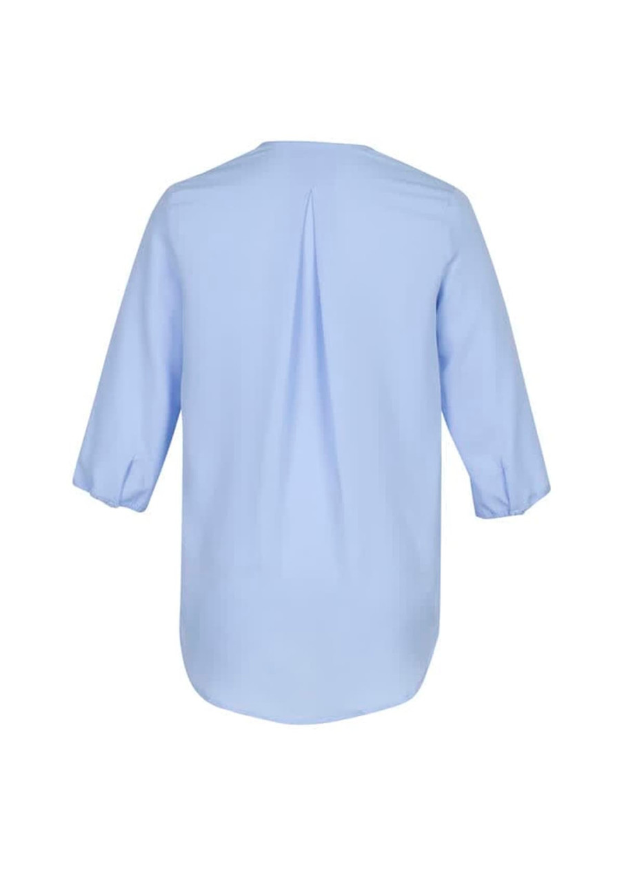 A light blue women's longline blouse featuring a back pleat and three-quarter sleeves. It has a logo visible.