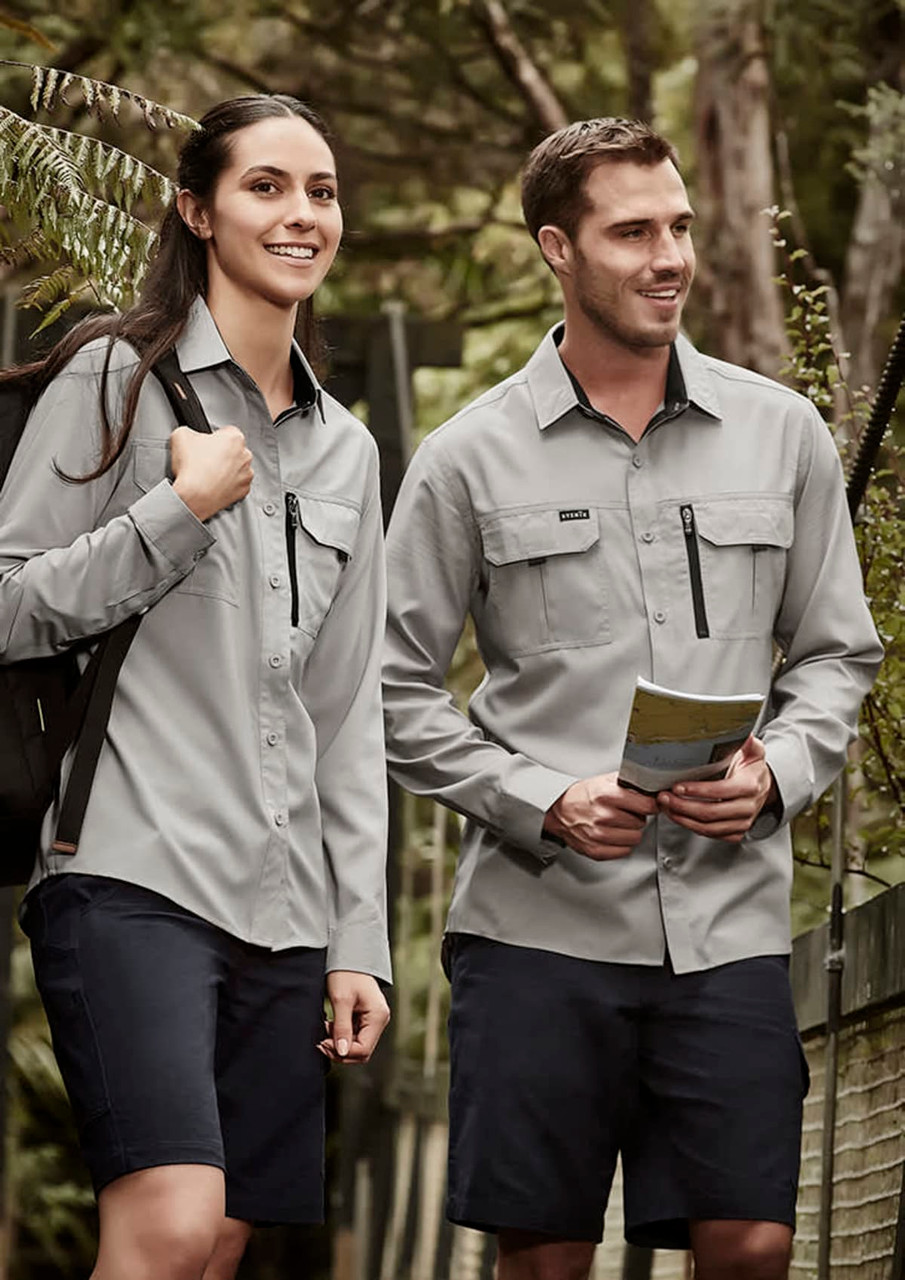 A man and woman wearing grey long sleeve button-up shirts with pockets, standing in a forested area.