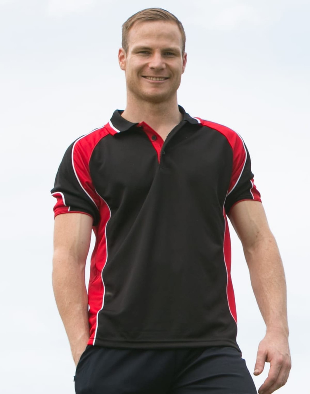 A men's polo shirt in black with red accents and a logo. The model is smiling and standing outdoors.