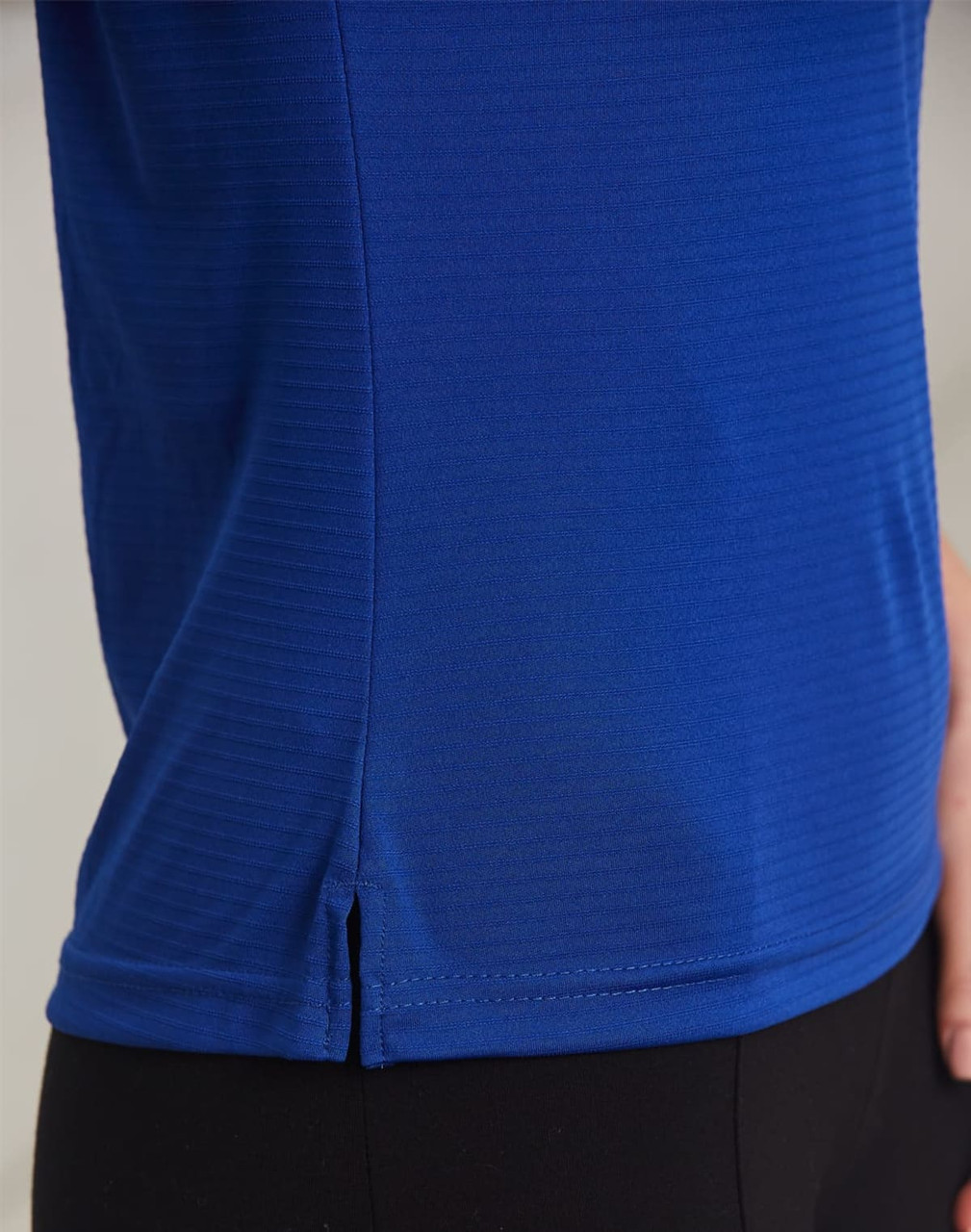 A close-up of a textured polo shirt in vibrant blue, featuring a small slit detail at the hem and a logo.