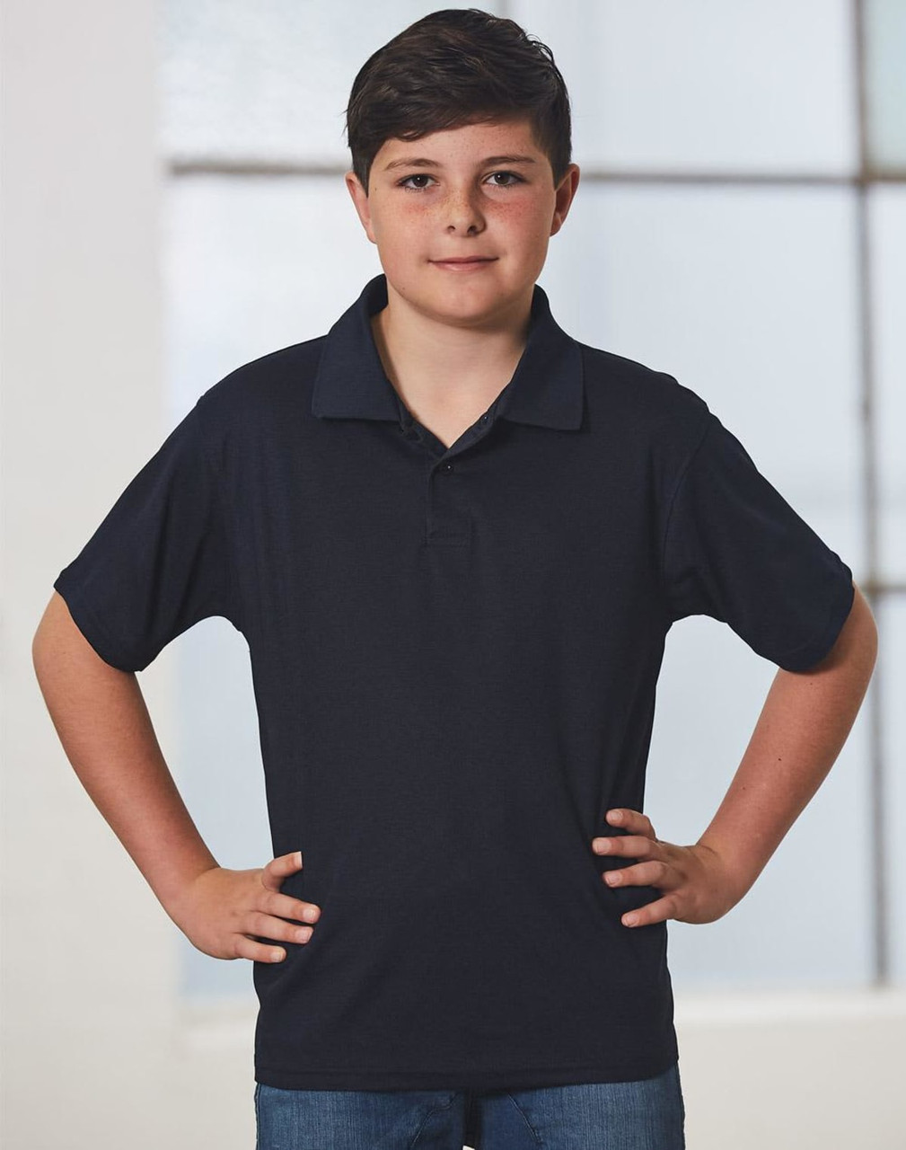 A young boy in a black short-sleeve polo shirt stands confidently with his hands on his hips.